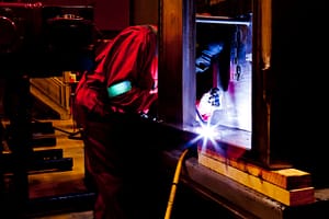A welder in a red suit skillfully working indoors with bright sparks and industrial equipment.